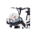 A small white dog in a basket liner on the front rack of a white ebike. 